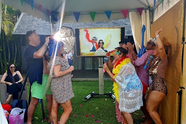 Photo Booth setup with golden backdrop and big screen with disguised people having fun at hotel
